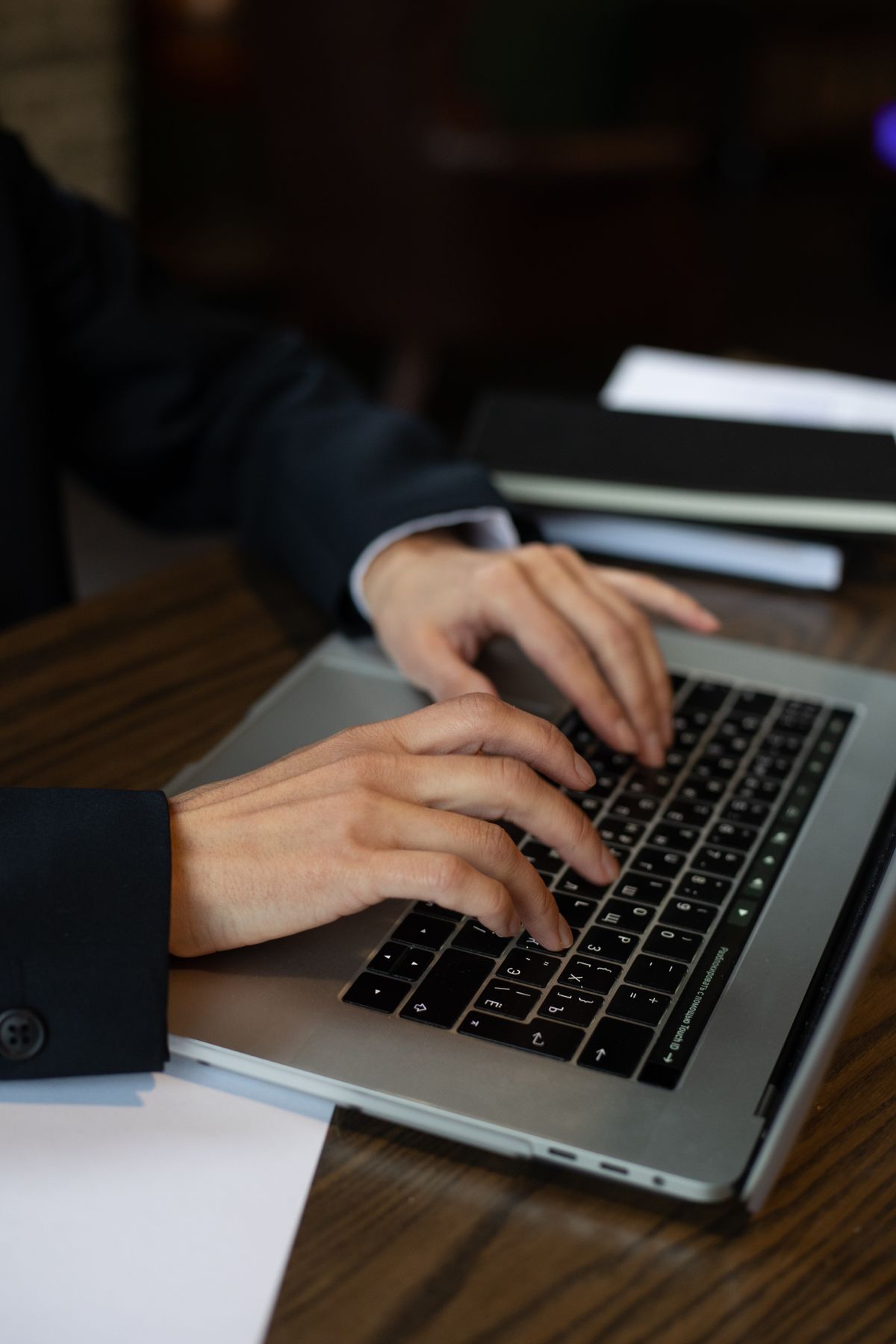 Hands typing on a laptop keyboard at a dark wooden desk